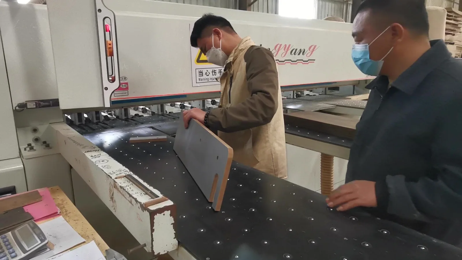 Two workers checking a drilled furniture panel at a production machine