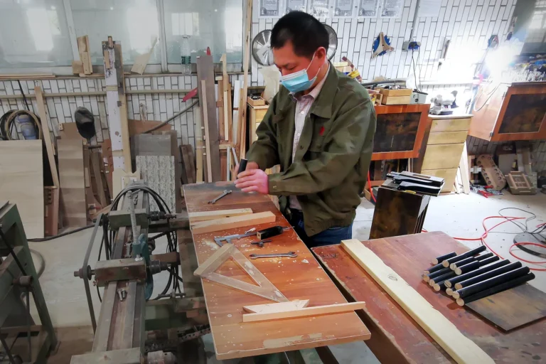 Worker measuring and marking a wooden furniture sample during quality inspection