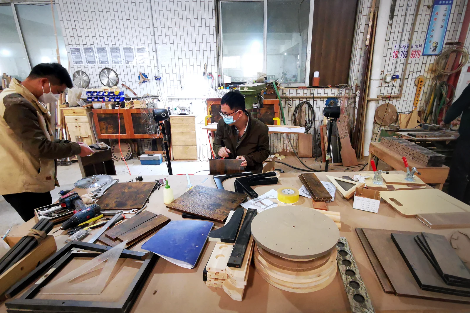 Two workers reviewing furniture samples and components at a workshop table